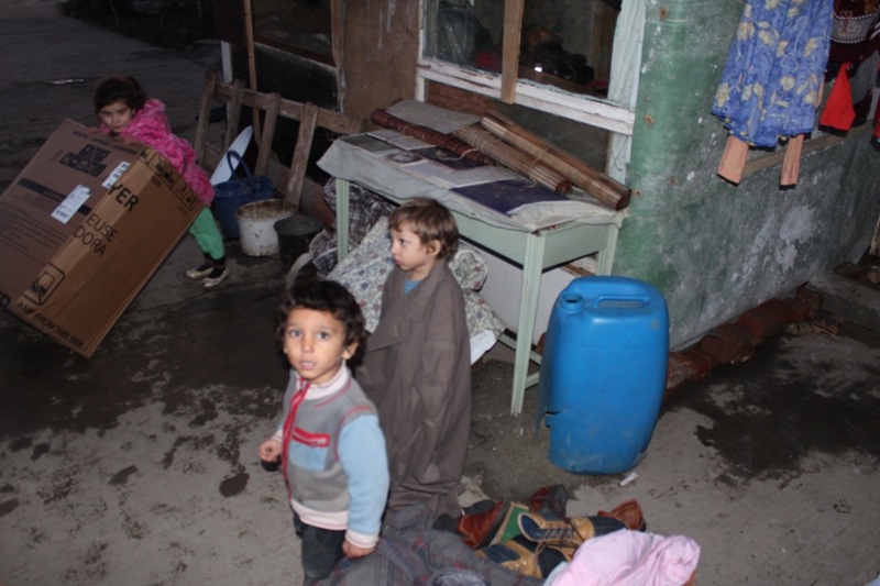 Two children standing in a room with trash.