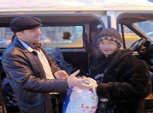 A man handing something to another person in the back of a car.