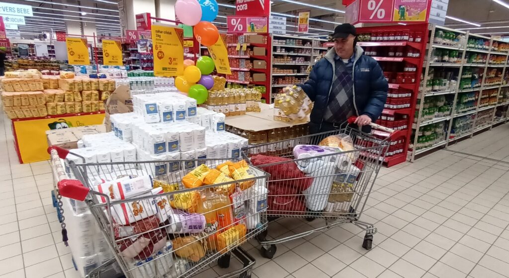A man pushing a cart full of food in a store.